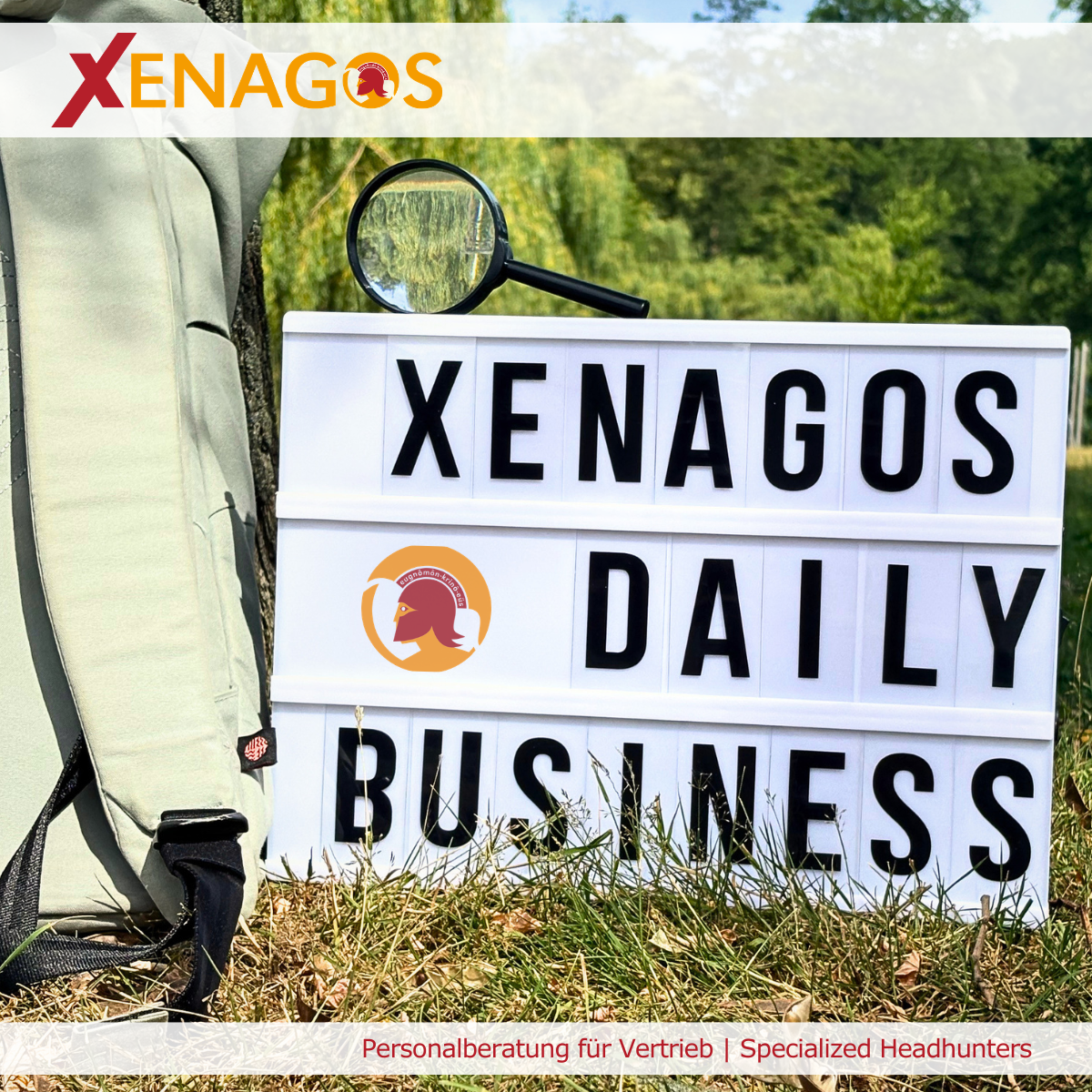 Leuchtschild mit der Aufschrift „Xenagos Daily Business“, daneben eine Lupe und eine Tasche im Grünen. Das Bild veranschaulicht den Blick hinter den Lebenslauf und die Bedeutung von Persönlichkeit bei der Besetzung von Vertriebspositionen.